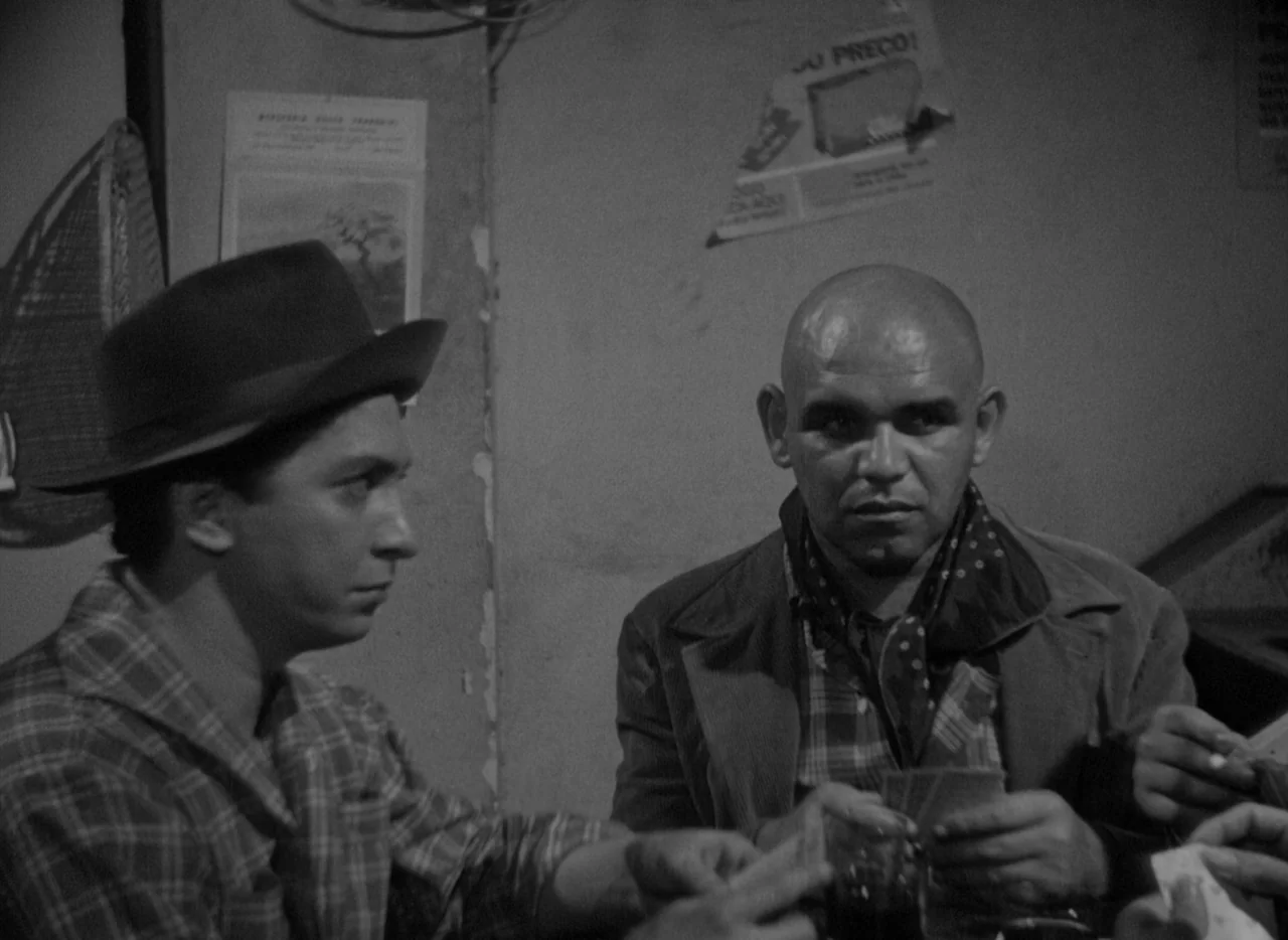 At Midnight I’ll Take Your Soul (1964) movie still: medium — A dimly lit room with paper posters on the wall featuring a card game. Two men sit at a…