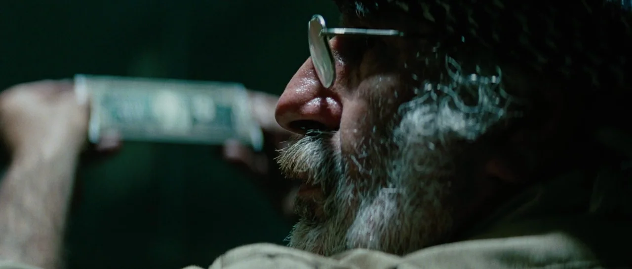 The A-Team (2010) movie still: closeup — A dimly lit room with dark surroundings hides most architectural detail. An elderly man with a white beard…