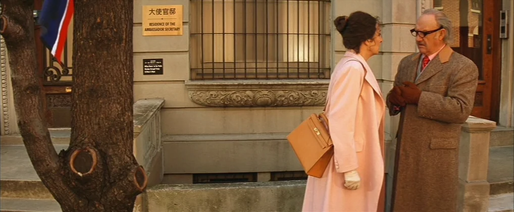 The Royal Tenenbaums (2001) movie still: fullbody — An exterior wall of a diplomatic building features a gold sign and window grate. A man and a…