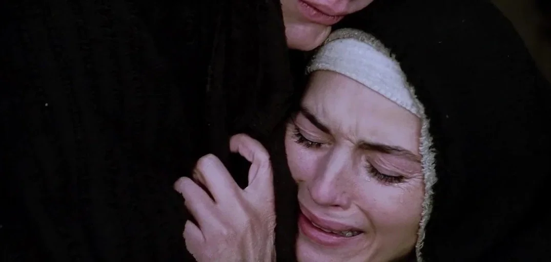 The Passion of the Christ (2004) movie still: closeup — A close-up view focuses on a woman crying while held by another figure. She wears a dark…