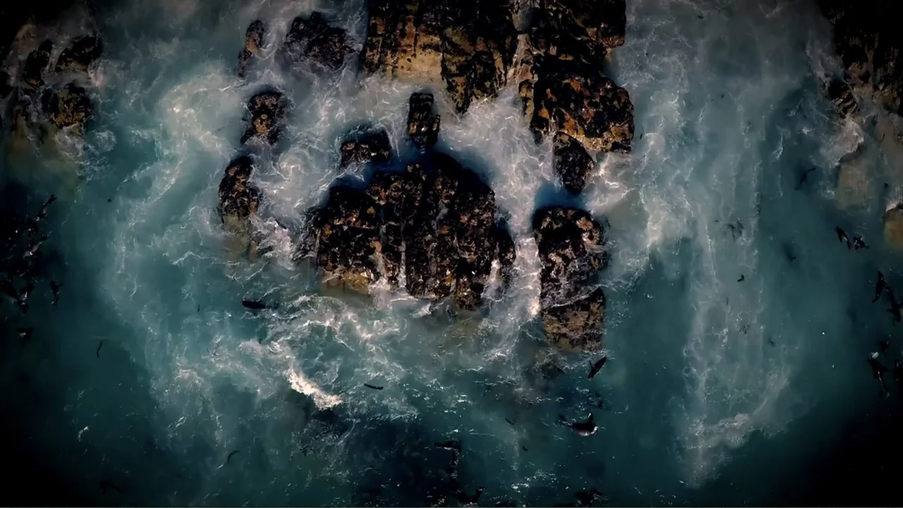 Air Jaws: Night Stalker (2016) movie still: establishing — A top-down view shows dark craggy rock formations surrounded by churning white sea foam.…