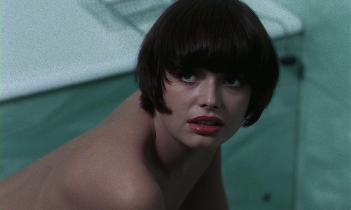 Daughters of Darkness (1971) movie still: closeup — A woman looks up inside a bathroom with teal-colored wall tiles. She is positioned partially out…