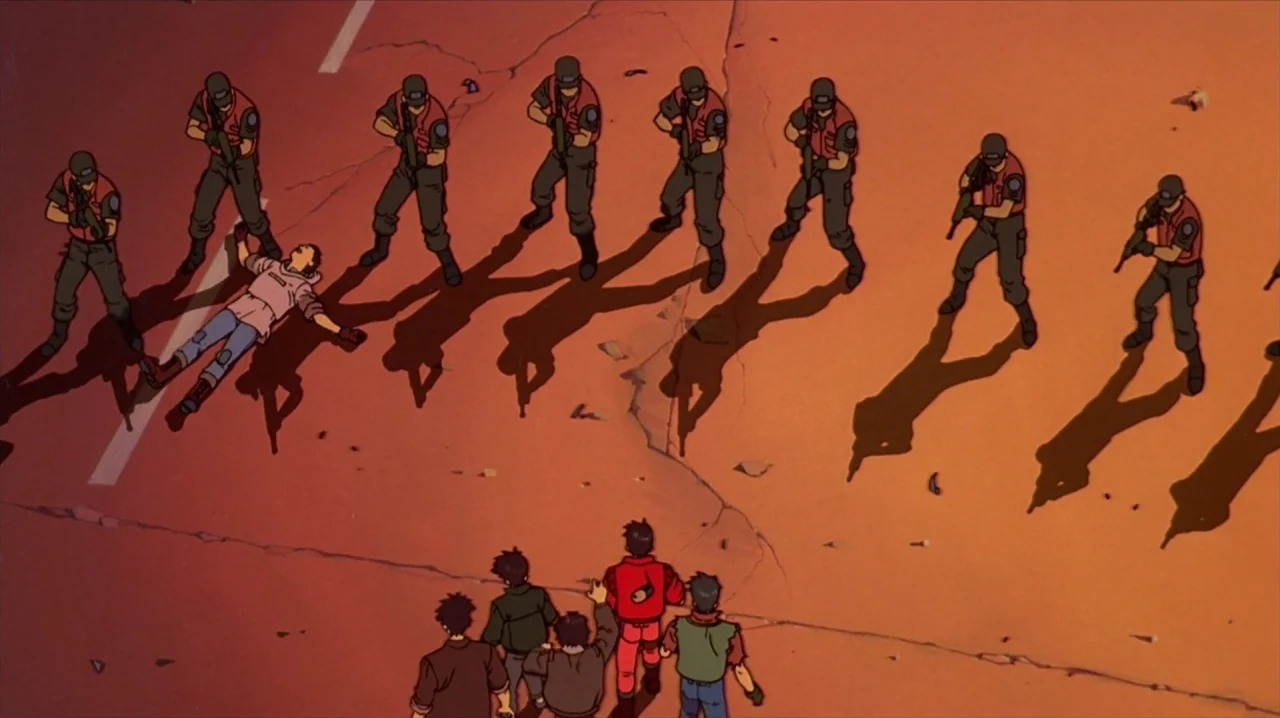 Akira (1988) movie still: wide — A cracked asphalt road surface displays long shadows cast by a line of armed soldiers. A group of individuals faces…