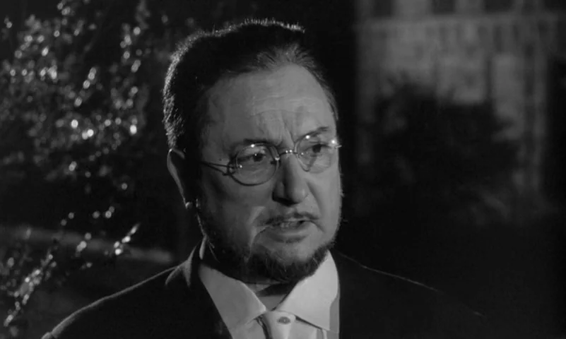 Eyes Without A Face (1960) movie still: closeup — A man stands outdoors at night with dark vegetation visible behind his head. He wears wire-rimmed…