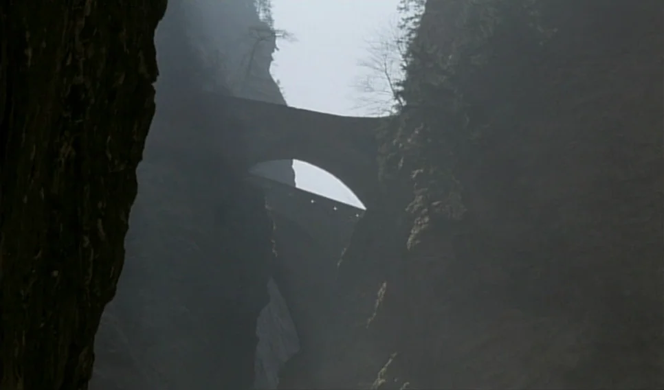 Heart of Glass (1976) movie still: establishing — A deep, narrow gorge with towering dark rock faces rises on both sides. Two arched stone bridges…