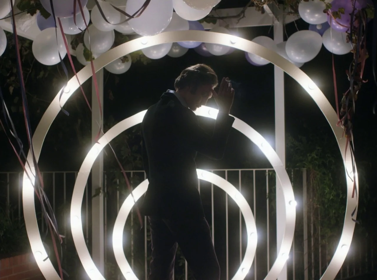 Girl Asleep (2015) movie still: medium — A night setting features circular glowing structures decorated with white balloons and ribbons. A man…