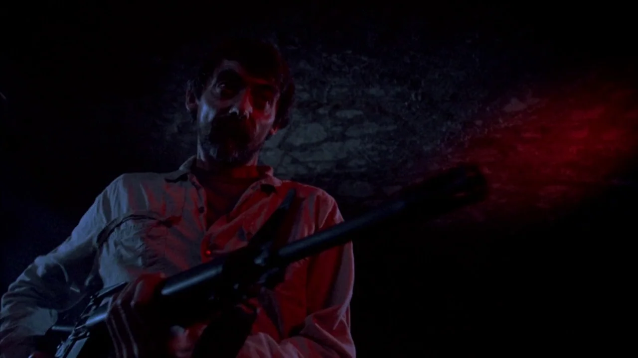 Day of the Dead (1985) movie still: medium — A dimly lit basement features a rough textured ceiling and shadow-heavy surroundings. A man with a dark…
