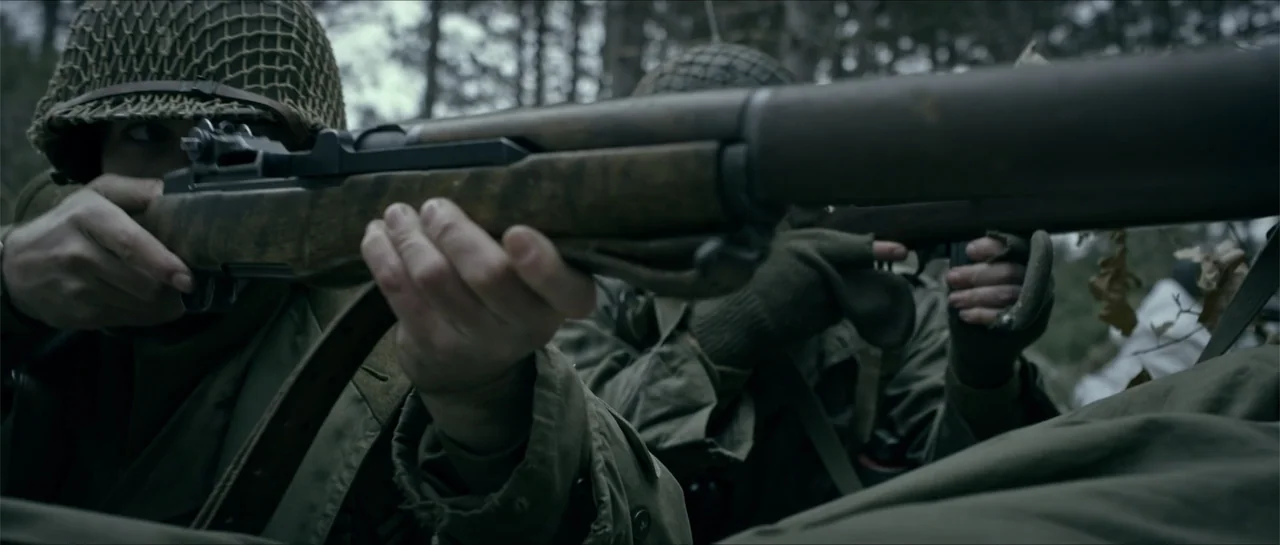Battle of the Bulge (1965) movie still: medium — A dense wooded area during daytime features soldiers in period military gear among trees. Two…