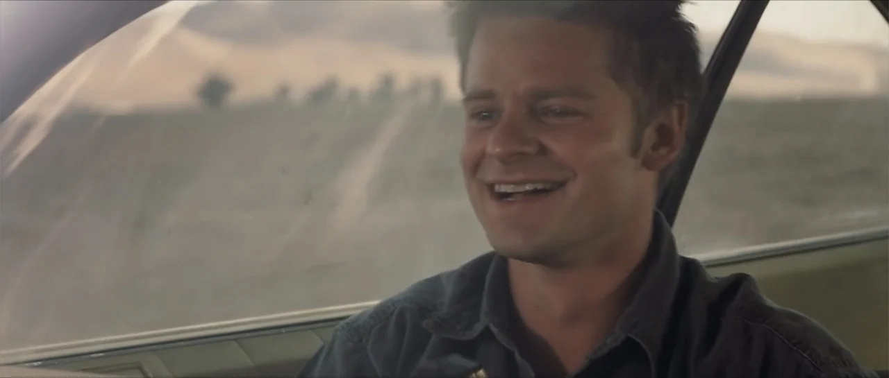 Joy Ride (2001) movie still: medium — A man is seated inside a moving vehicle traveling through a desert landscape. The subject turns his head and…