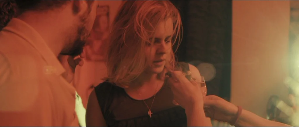 Lasting (Nieulotne) (2013) movie still: medium — A dimly lit room with intense red lighting tones and hazy lens flares. A young woman holds a small…