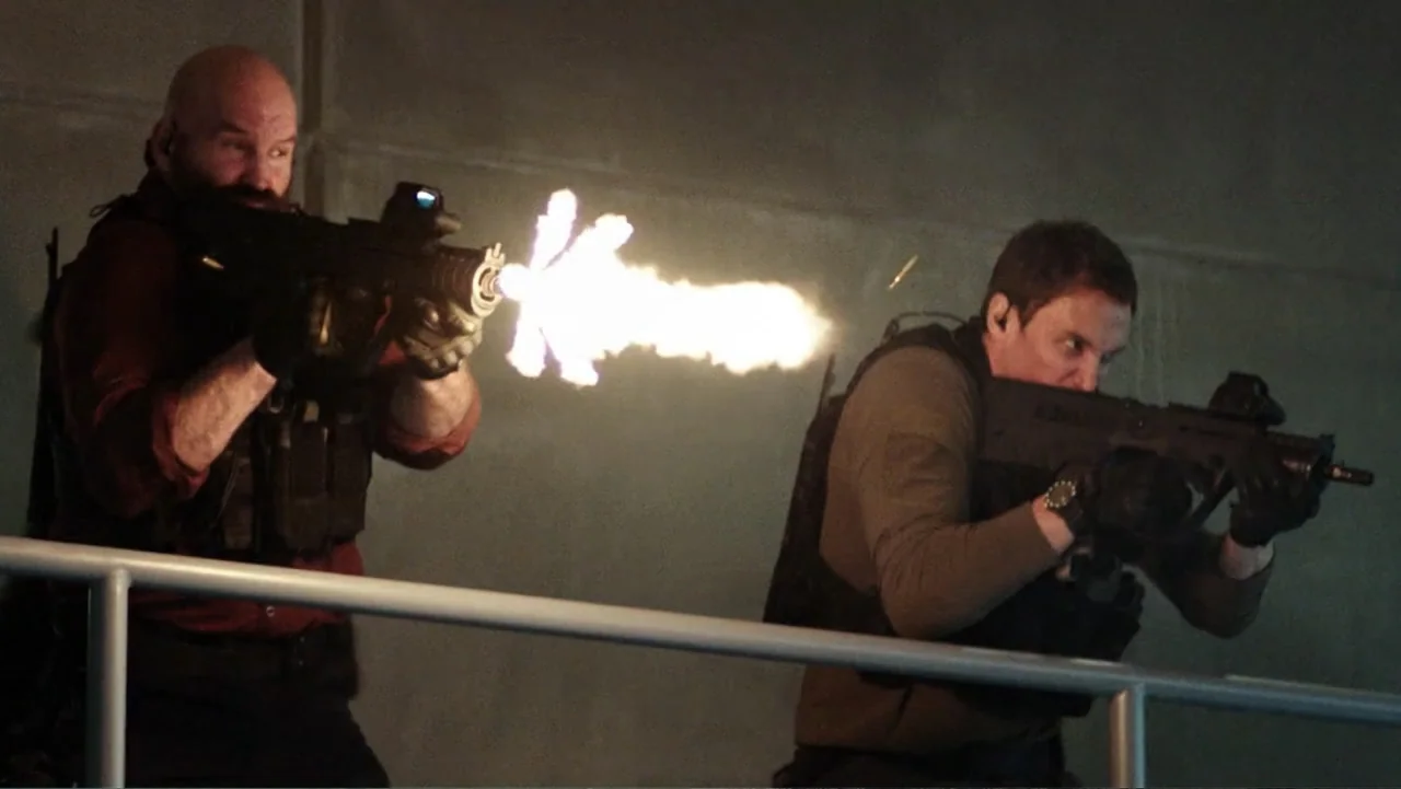 Skyscraper (2018) movie still: medium — Two men stand on a grey industrial catwalk behind a simple metal railing. The men fire tactical rifles while…
