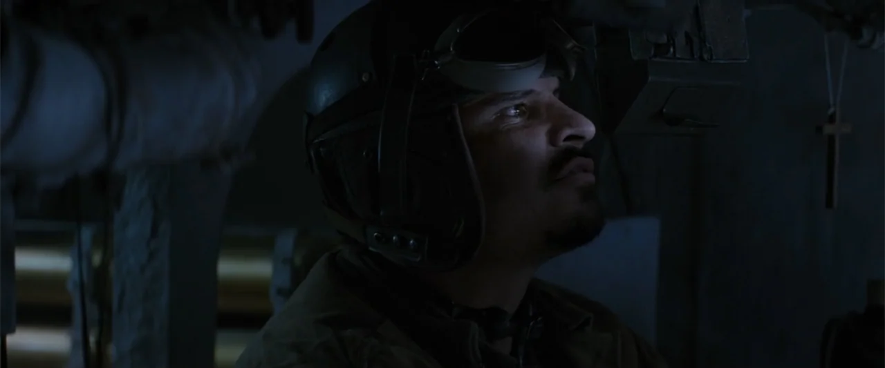 Fury (2014) movie still: closeup — A dark, cramped interior of a metal submarine compartment filled with pipes. A man wearing a leather flight…