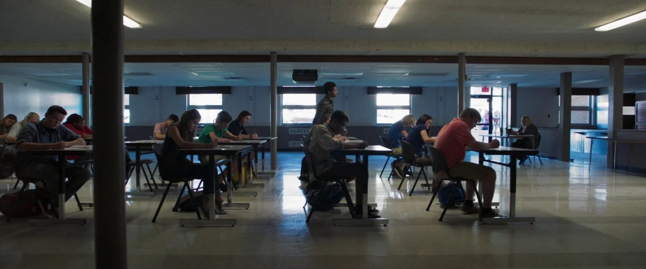 Mom and Dad (2017) movie still: wide — A large, open hall serves as a makeshift testing center with rows of tables. Multiple students sit at…