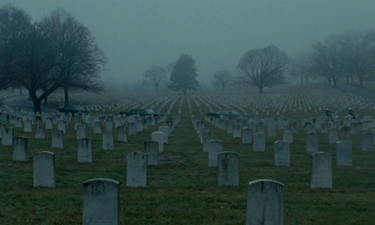Jackie (2016) movie still: establishing — A vast military cemetery features rows of identical white stone markers under gray skies. Several dark…