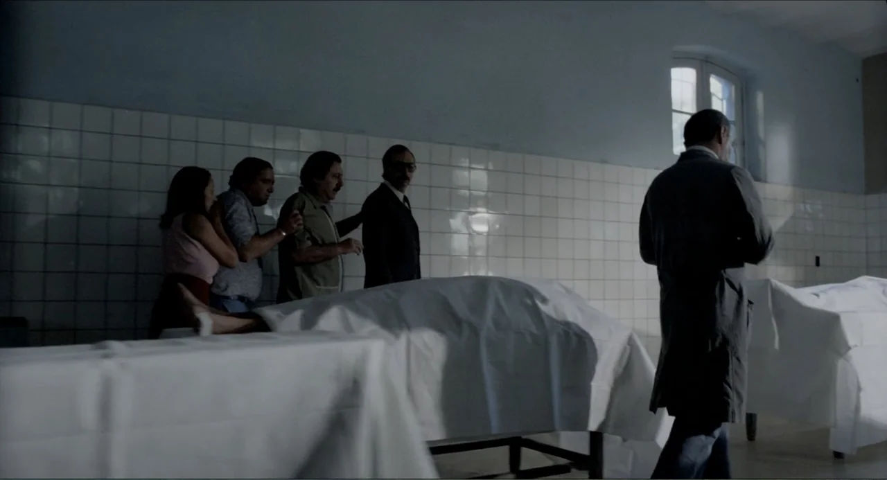 Waiting for the Hearse (1985) movie still: wide — A sterile room features white tiled walls and multiple gurneys covered by white sheets. Five…
