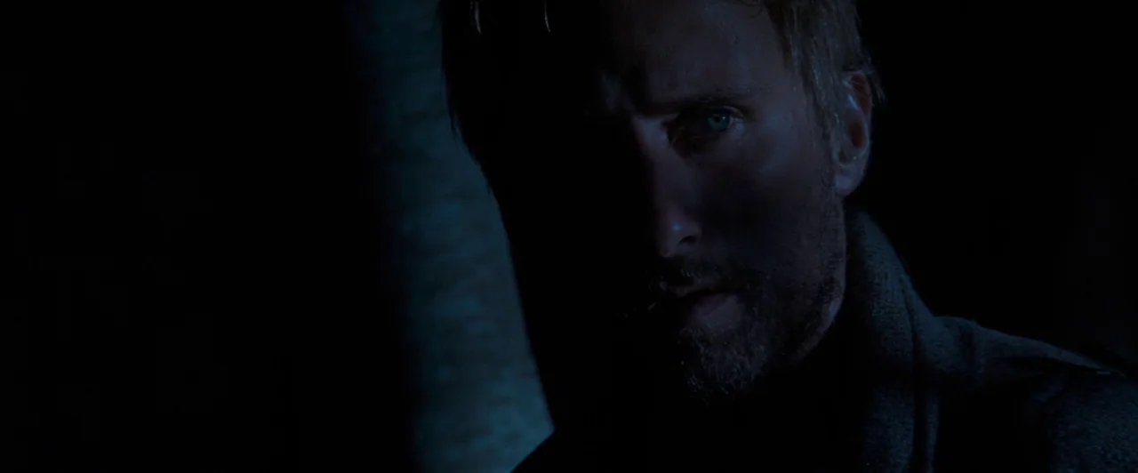 Far from the Madding Crowd (2015) movie still: closeup — A man stands in a dark environment with trees partially visible to the left. He looks into…