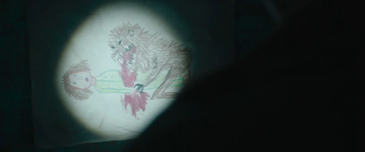 Wildling (2018) movie still: closeup — A dark environment is partially lit by a concentrated beam from a flashlight. The light falls upon a crude…