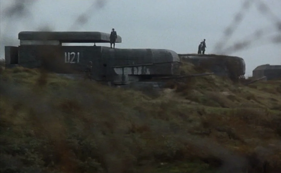 Soldier of Orange (1977) movie still: wide — A set of heavy concrete bunkers sits on a grassy, wind-swept coastal ridge. Three soldiers stand atop…
