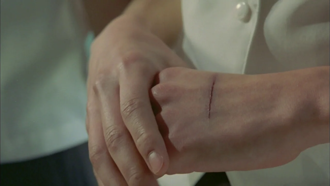Whispering Corridors (1998) movie still: closeup — Close-up of a person's pale hands resting against white fabric clothing. One hand displays a…