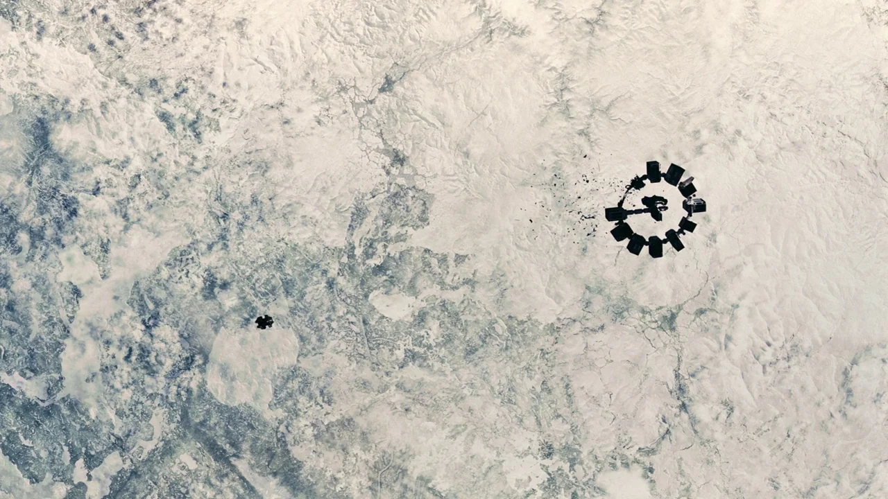 Interstellar (2014) movie still: establishing — An aerial view displays a vast, snow-covered landscape with rugged, frozen terrain features. A large…