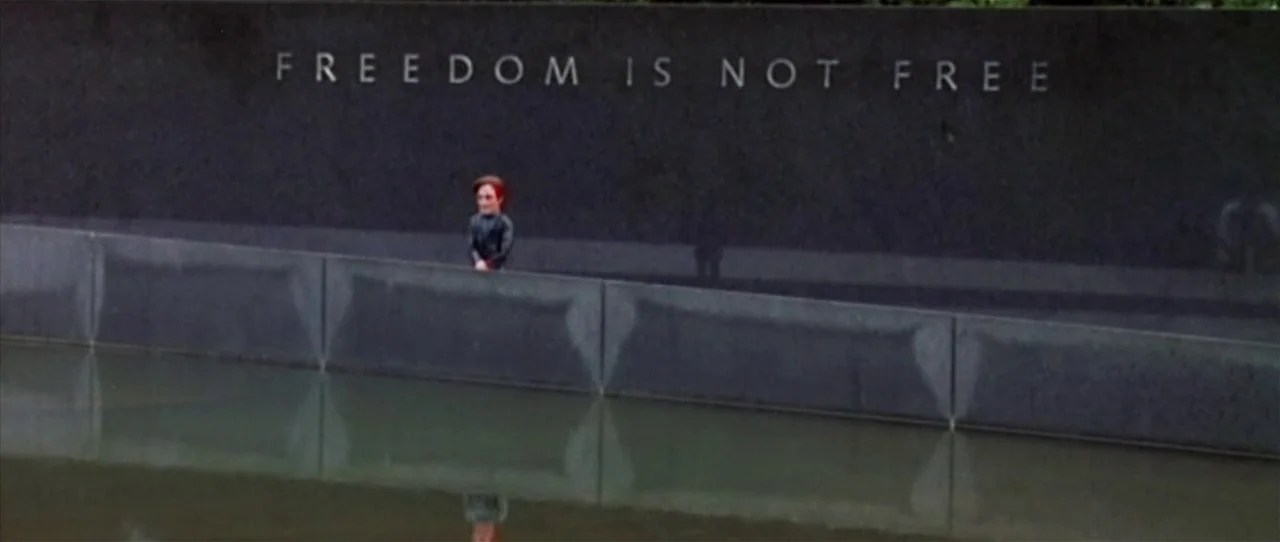 Team America: World Police movie still: wide — A polished black granite memorial wall with engraved lettering sits above a reflective pool. A small…
