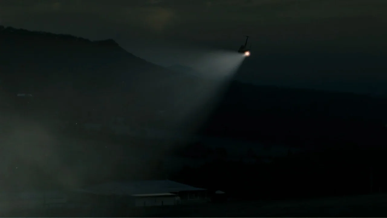 Tomorrow, When the War Began (2010) movie still: wide — A dark, mountainous landscape is illuminated by an overhead spotlight at night. A helicopter…
