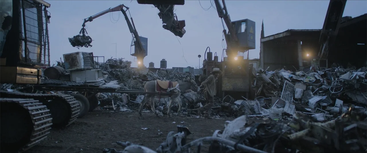 Radical (2023) movie still: wide — A vast scrapyard filled with piles of discarded metal and heavy industrial machinery.