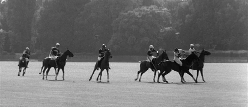 Les Amants (1958) movie still: wide — A wide shot shows several polo players riding horses across an open grassy field. Thick green trees are…
