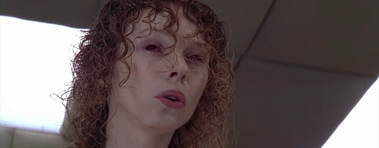 Event Horizon (1997) movie still: closeup — The interior of a sterile medical facility with drop ceiling tiles. A woman with wet-looking, curly…