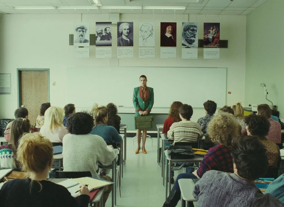 Laurence Anyways (2012) movie still: wide — A brightly lit, beige-toned university classroom with multiple students seated at desks facing forward.…