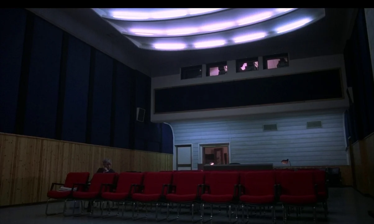 Cinema Paradiso (1988) movie still: wide — A modern screening room features rows of empty red chairs against navy acoustic panels. A curved ceiling…