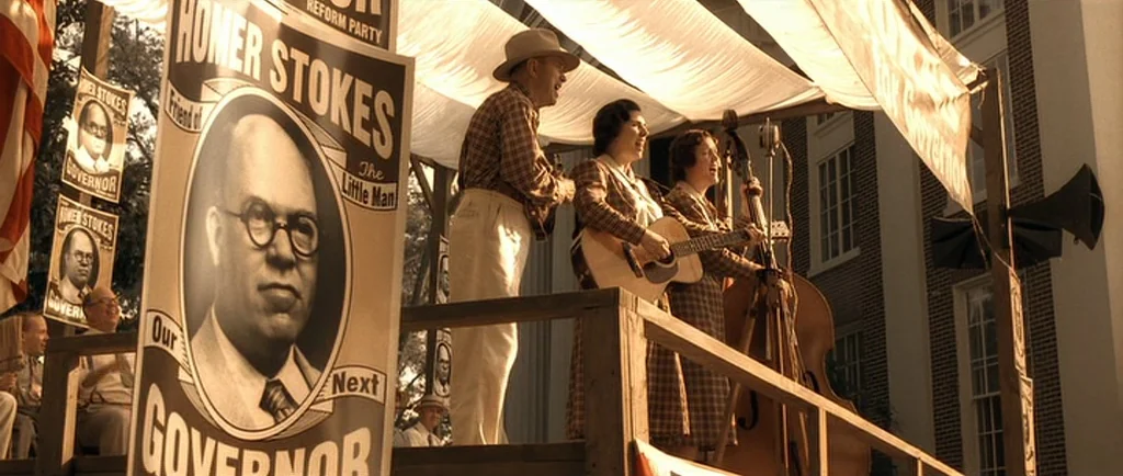 O Brother, Where Art Thou? (2000) movie still: wide — A wooden political stage is decorated with posters for a gubernatorial candidate named Homer…