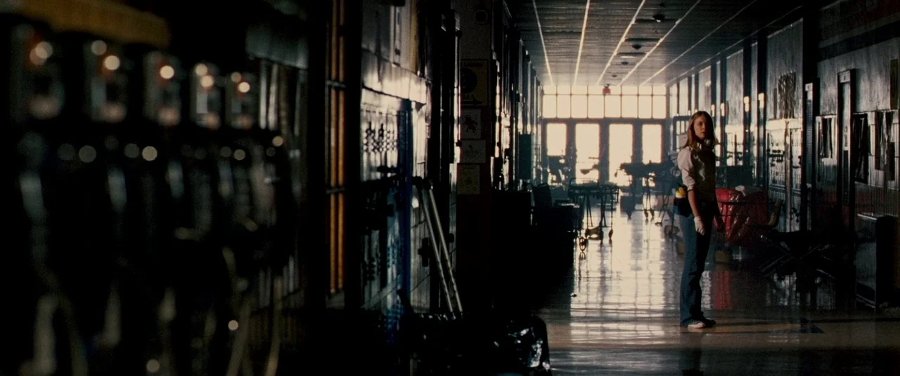 Carriers (2009) movie still: wide — A long, dark school corridor features rows of lockers and linoleum floors reflecting the light. A lone woman…