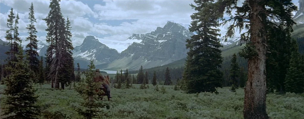 River of No Return (1954) movie still: wide — A sprawling mountain valley features dense pine forests and snow-capped peaks in the distance. A…