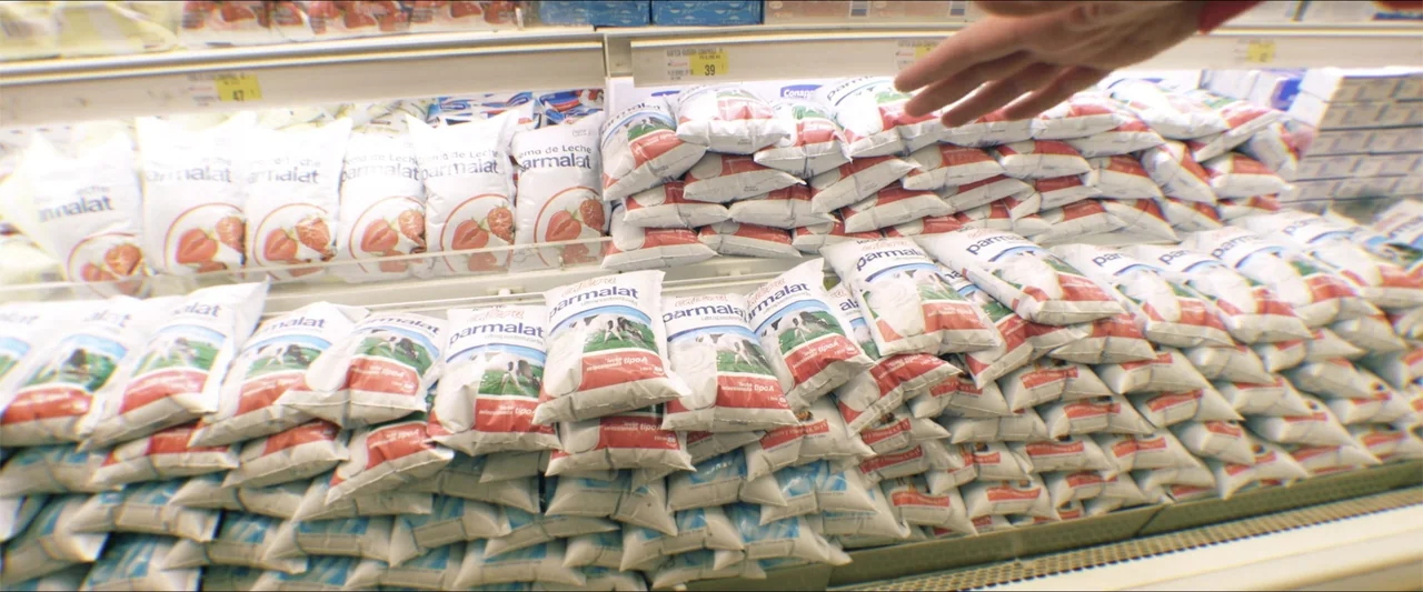 High Five (2004) movie still: medium — A supermarket refrigerated display case is densely stocked with rows of bagged dairy products. A human hand…