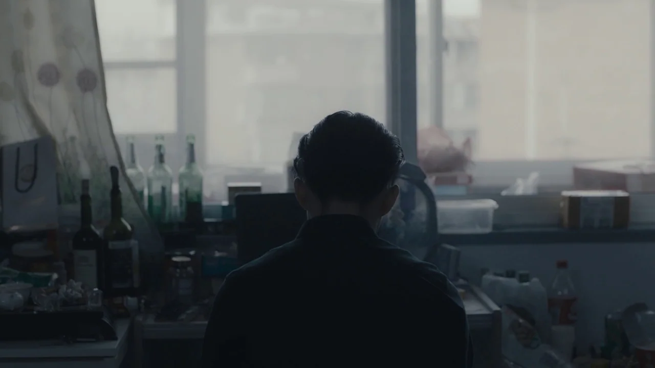 An Elephant Sitting Still (2018) movie still: medium — A cluttered apartment desk sits in front of a window overlooking a hazy urban area. A person…