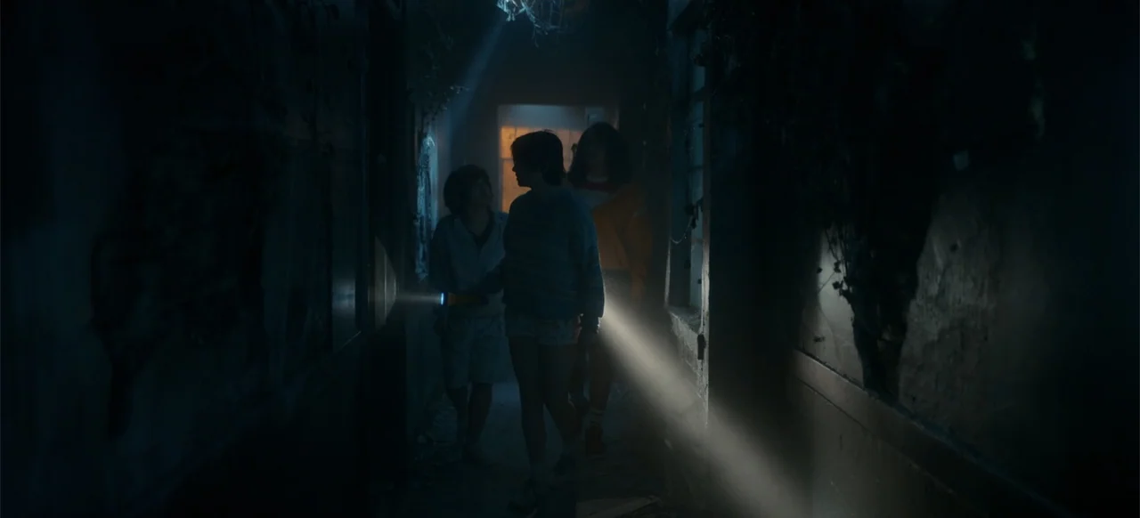 My Best Friend's Exorcism (2022) movie still: medium — A dilapidated, narrow passage features peeling walls and debris under low-key lighting. Three…