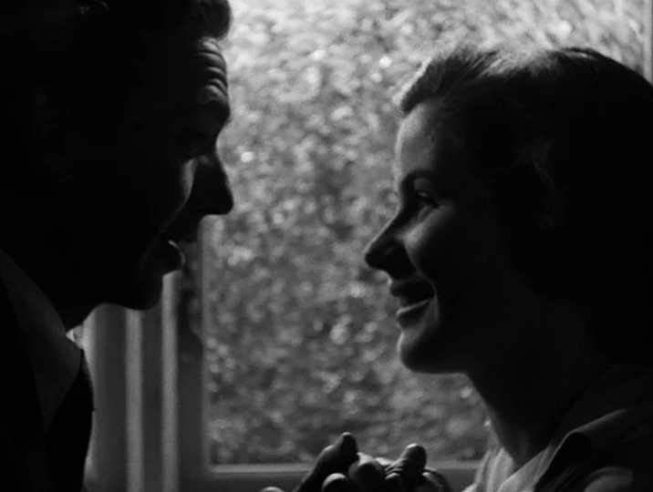 To Joy (1950) movie still: closeup — A dark indoor space defined by a glowing, out-of-focus window in the center. A man and a woman stand close…