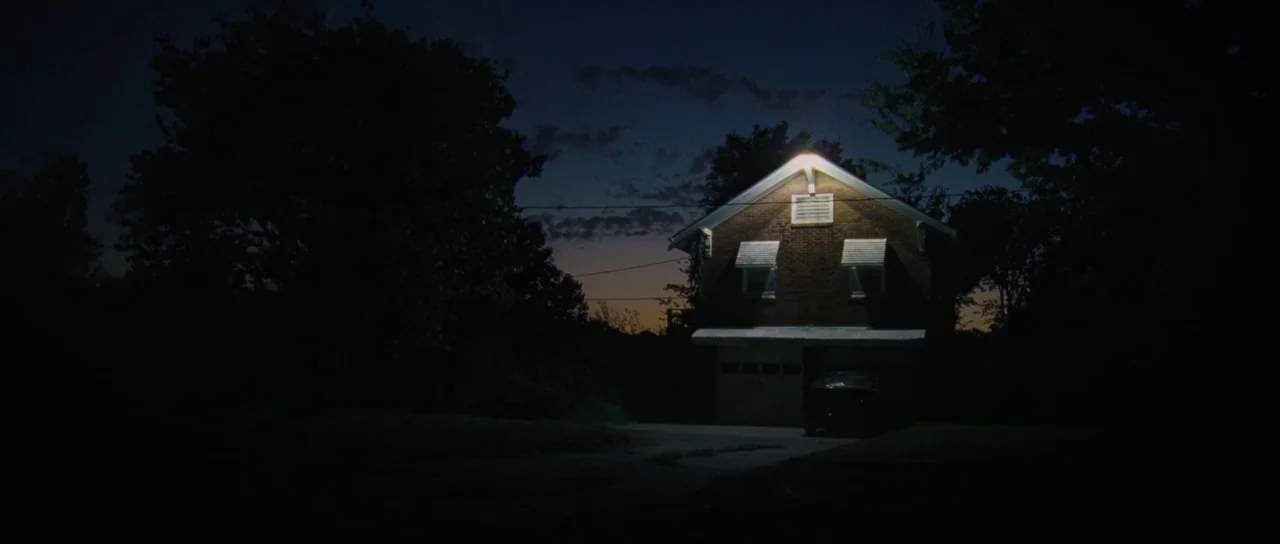 To The Wonder (2012) movie still: establishing — A dark brick two-story house stands isolated against a dark twilight horizon. A single exterior…