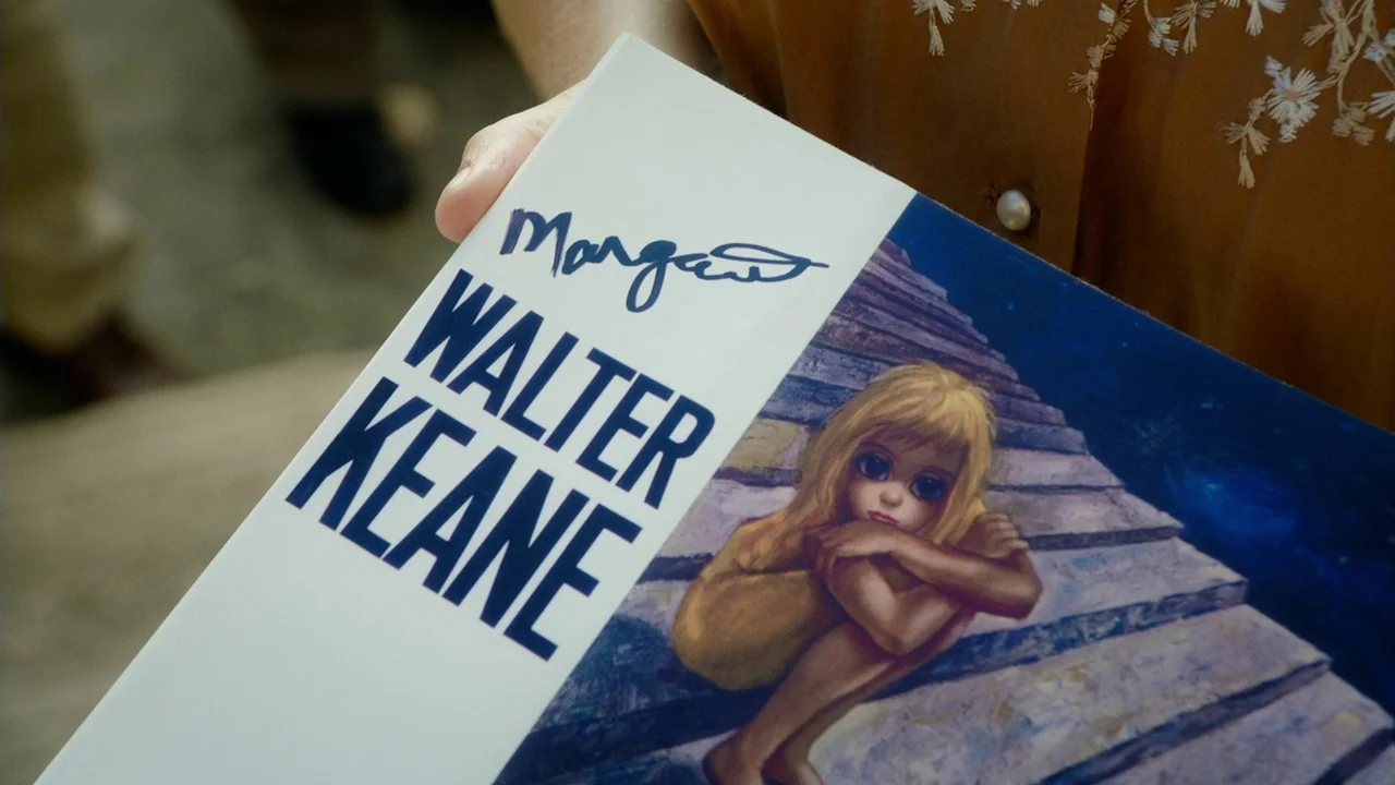 Big Eyes (2014) movie still: closeup — A close-up shows a white book cover titled Walter Keane with a signature. A hand holds the book in front of a…