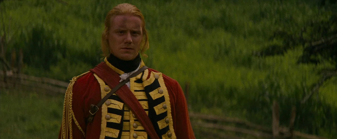 The Last of the Mohicans (1992) movie still: medium — A man in a 18th-century British military uniform stands in a grassy field. He is positioned in…