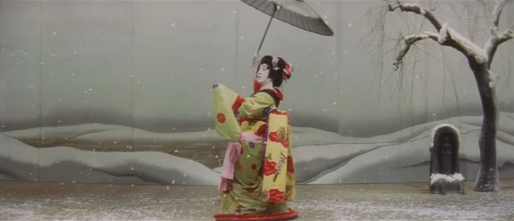 An Actor’s Revenge (1963) movie still: fullbody — A theatrical stage set features a painted backdrop of a snowy winter landscape. A performer in a…