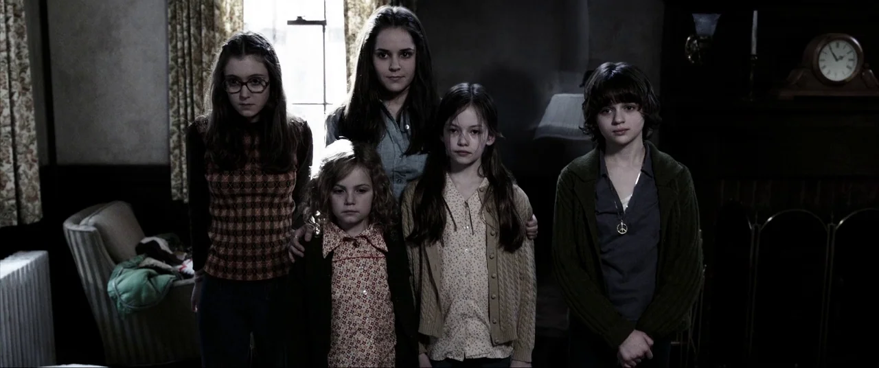 The Conjuring (2013) movie still: medium — A dimly lit room with a fireplace and wood-paneled walls in the background. Five children stand in a line…