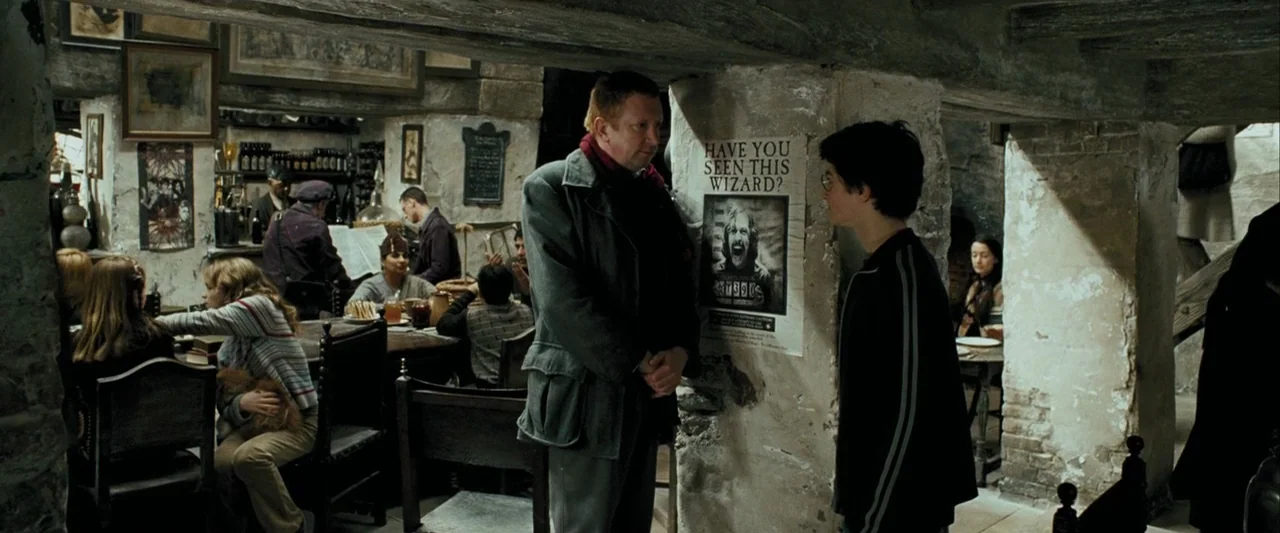 Harry Potter and the Prisoner of Azkaban (2004) movie still: medium — A dimly lit pub with stone walls and wooden furniture hosts several patrons. A…