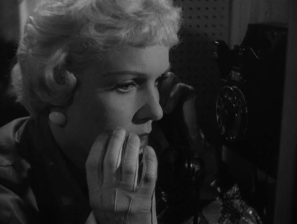 Dreams (1955) movie still: closeup — A cramped and dark interior space featuring a vintage wall-mounted rotary telephone. A blonde woman in gloves…