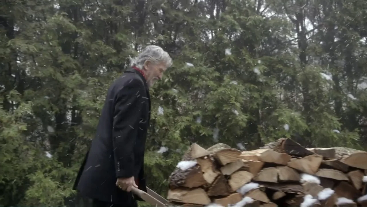 The Christmas Cure (2017) movie still: medium — An elderly man works in a backyard filled with evergreen trees during winter. He loads split…