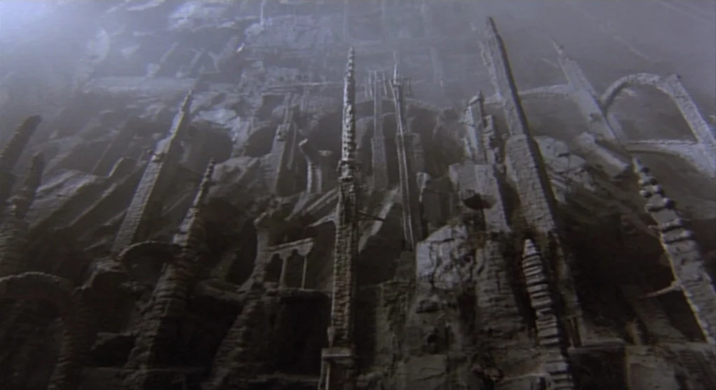 Time Bandits (1981) movie still: establishing — An immense, craggy stone structure looms upward into a thick, obscuring gray fog. Sharp vertical…