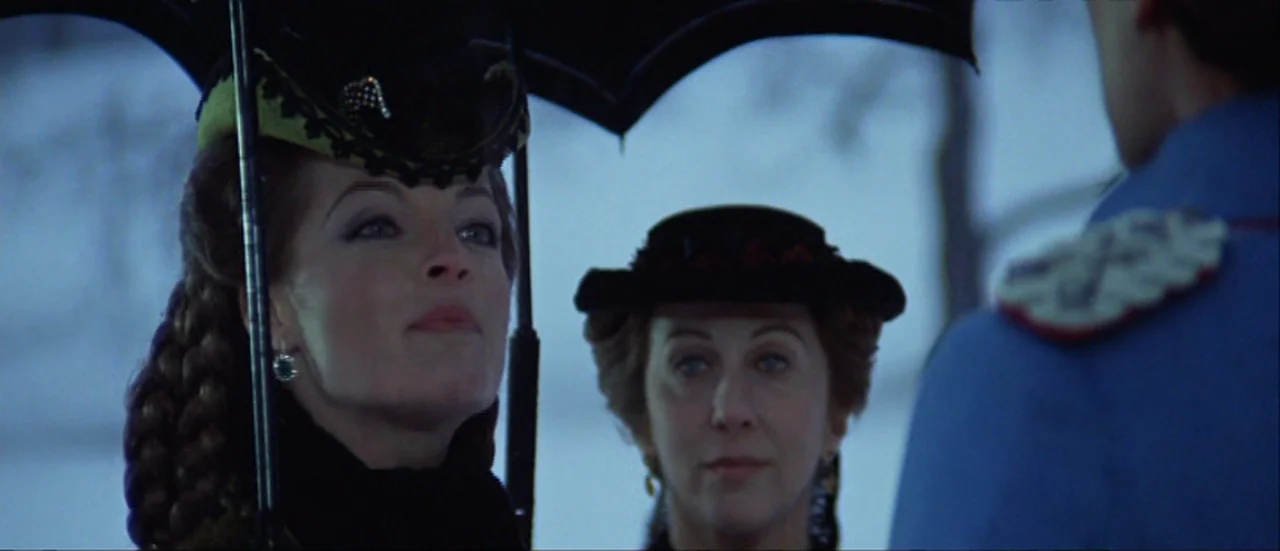 Ludwig (1973) movie still: medium — An outdoor setting with a blurred background showing a snowy landscape under overcast sky. Two women dressed in…