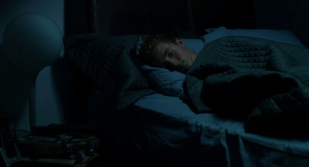Maps to the Stars (2014) movie still: medium — A darkened room features a person sleeping in a bed with gray linens. A spherical lamp on a…