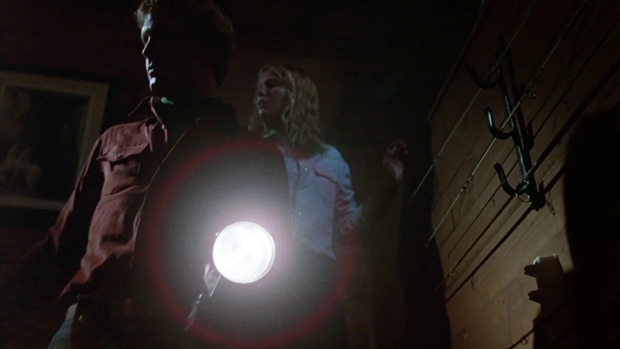 Friday the 13th Part 2 (1981) movie still: medium — The interior of a wooden cabin features walls lined with hooks for fishing gear. A man holds a…